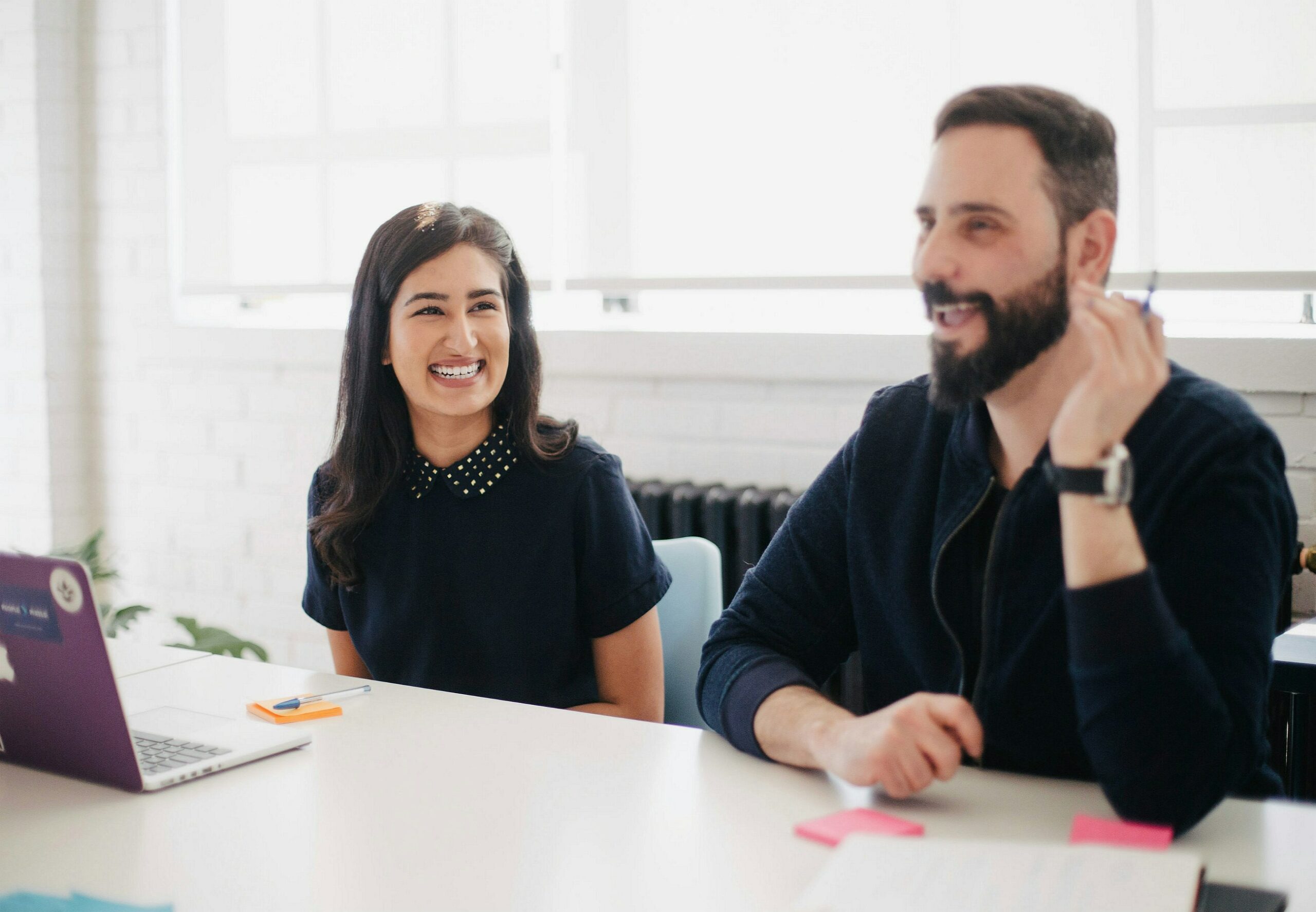 Two coworkers sitting, smiling, and talking in an office