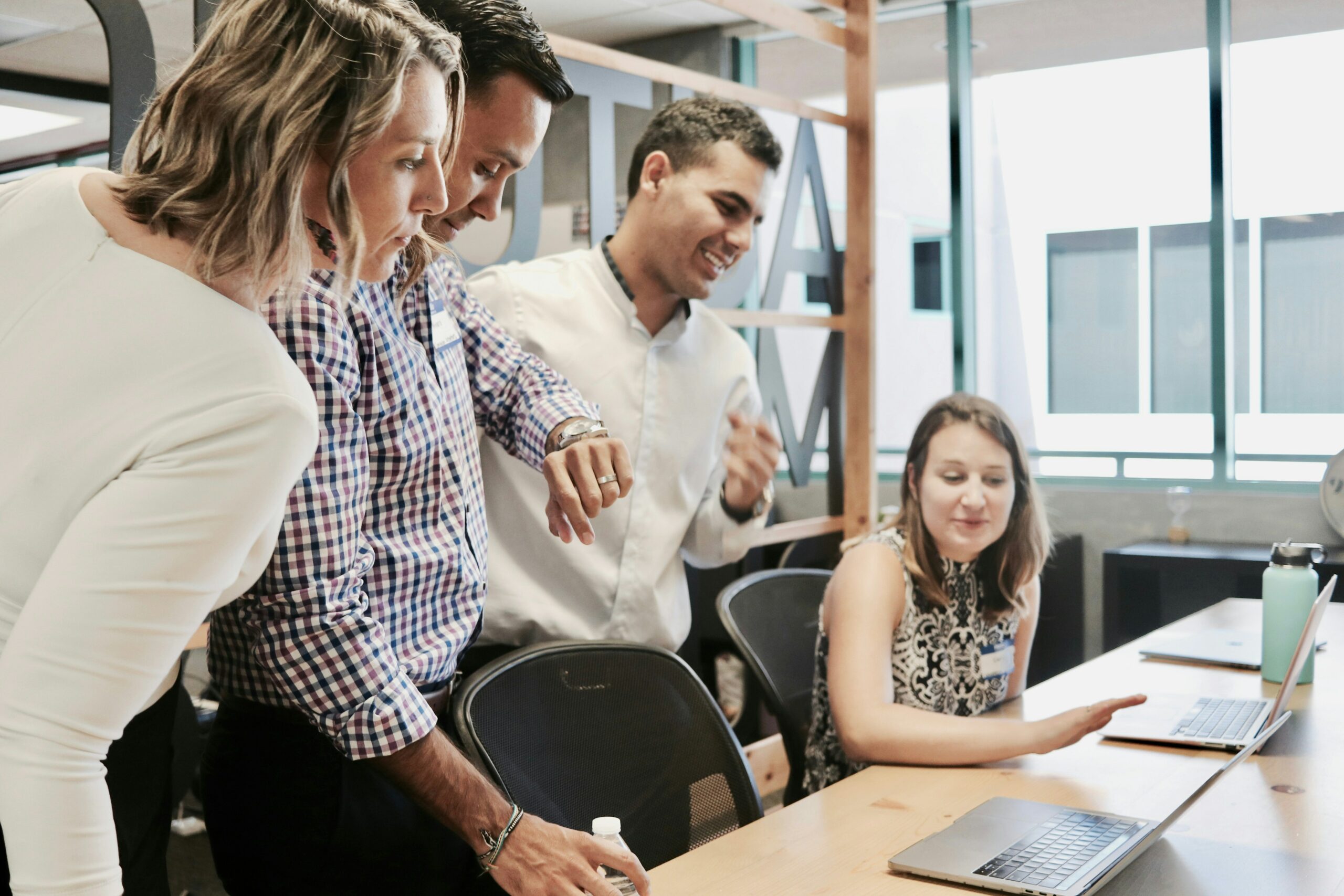 A group of four coworkers reviewing work on a laptop at a desk