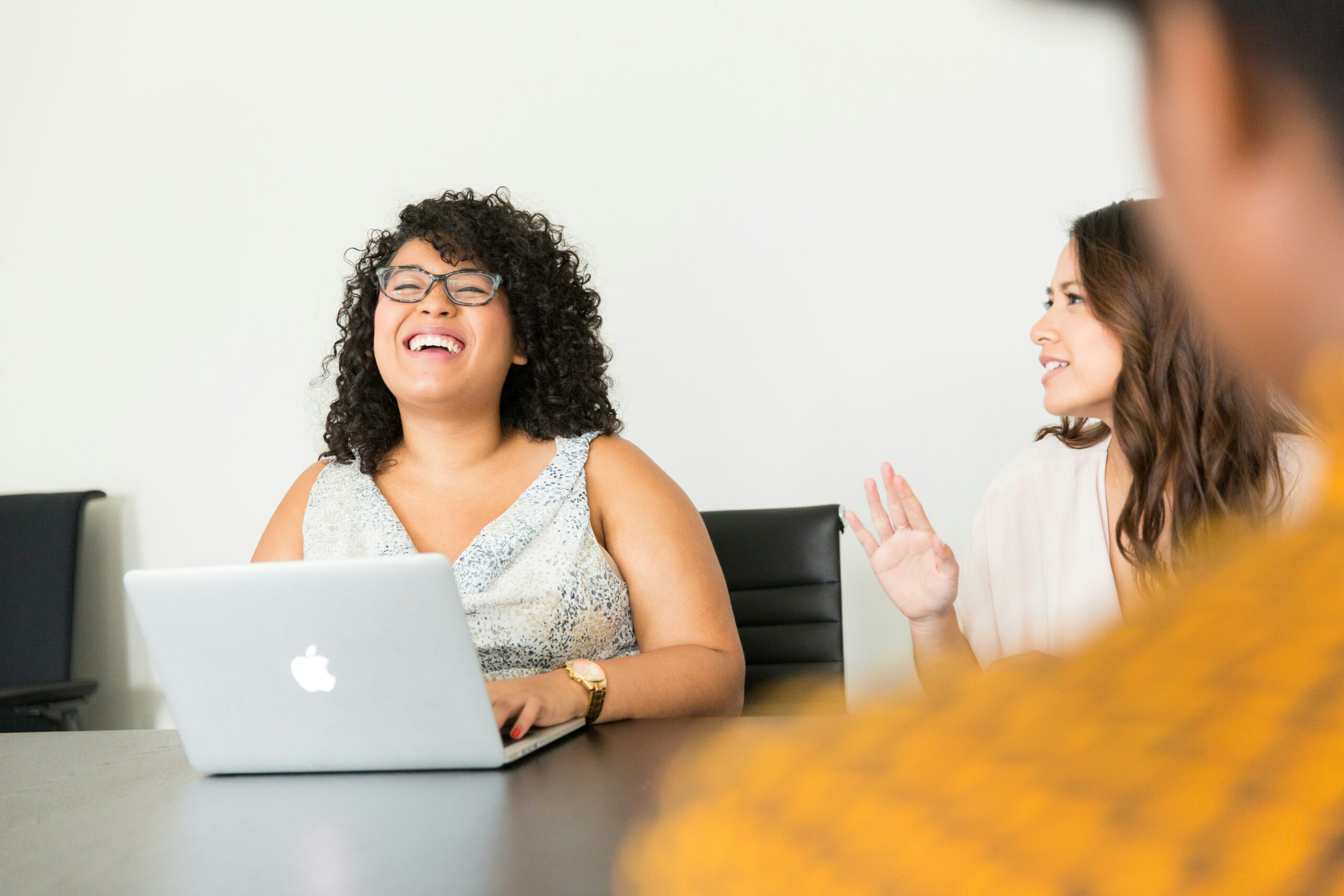 A woman on her laptop laughing at a desk with coworkers